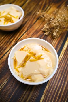 two white bowls filled with ice cream on top of a wooden table next to dried flowers