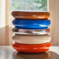 a stack of different colored plates sitting on top of a table next to a window