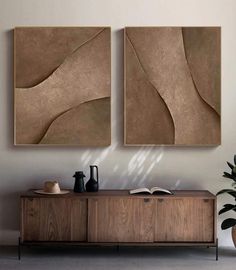 two abstract paintings on the wall above a wooden sideboard with a plant in it