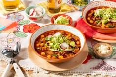 two bowls filled with chili and beans on top of a table next to utensils