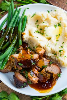 meat, mashed potatoes and green beans on a white plate with garnish