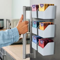 a person's hand is pointing at the magnets on a refrigerator that has several different colored packets in it