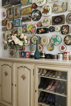 a wall full of plates and vases on top of a wooden table next to a cabinet