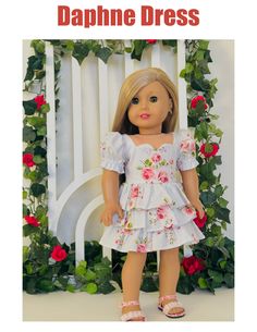 the doll is wearing a white dress with flowers on it, and has pink shoes