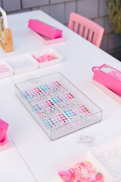 the table is set up with pink and white decorations on it, including square trays filled with confetti sprinkles