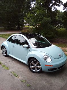 a light blue car parked on the side of a road next to some grass and trees