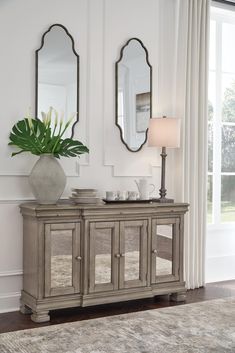 a white vase sitting on top of a wooden table next to a mirror and lamp