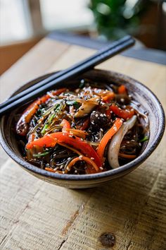 a bowl filled with vegetables and chopsticks sitting on top of a wooden table