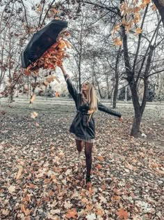 a woman holding an umbrella while standing in the middle of autumn leaves on the ground