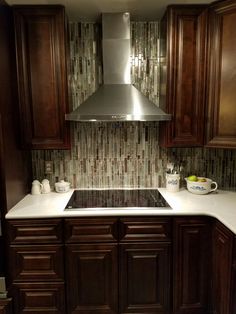 a kitchen with dark wood cabinets and white counter tops, stainless steel hood over the stove