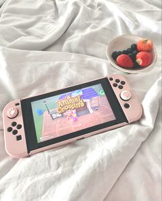 a pink nintendo wii game system sitting on top of a bed next to some fruit