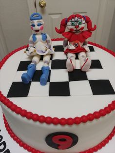 two toy figures sitting on top of a checkerboard cake with red icing