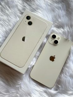 two iphones sitting next to each other on top of a white fur covered surface