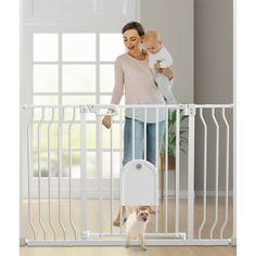 a woman holding a baby in her arms and standing next to a white metal gate