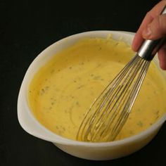 a whisk in a white bowl filled with yellow sauce on a black surface