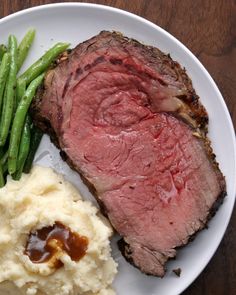 a white plate topped with meat, mashed potatoes and green beans on top of a wooden table