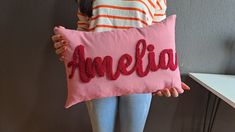 a woman holding a pink pillow with the word amelie on it in red sequins