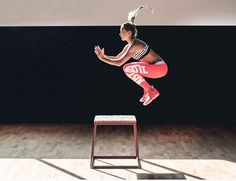 a woman jumping up in the air on top of a wooden floor next to a stool