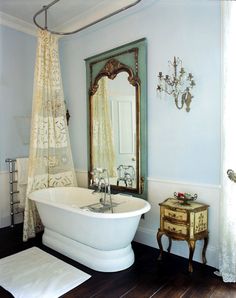 a white bath tub sitting next to a mirror and wooden floor in a bathroom under a chandelier