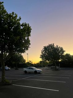 a car parked in a parking lot next to a tree at sunset or dawn with the sun going down