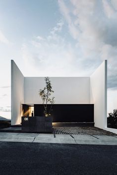 an empty white building with a tree in the front and sky behind it on a cloudy day