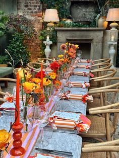 a long table is set with orange and yellow flowers in vases, candles, and napkins