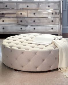 a white round ottoman sitting on top of a floor next to a dresser and mirror