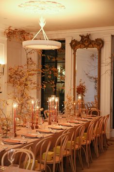 a long table with many chairs and candles on it in front of an ornate mirror