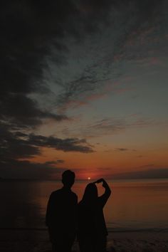 two people standing on the beach at sunset