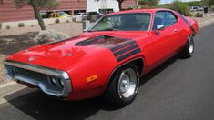 a red muscle car parked on the side of the road