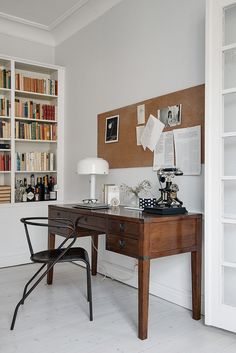 a desk with a chair, lamp and bookshelf in the background on a white floor