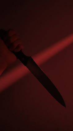 a person holding a knife in the dark with red light coming from behind it,