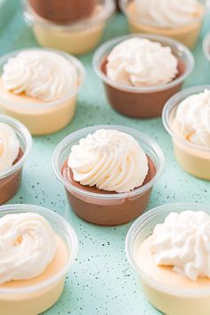 cupcakes with white frosting in plastic cups on a blue tableclothed surface