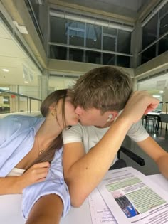 a young man and woman kissing while sitting at a table in front of a laptop computer