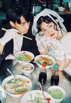 two people sitting at a table with bowls of food and chopsticks in their hands