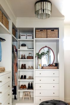 a white closet with lots of shoes and other items on shelves next to a round mirror