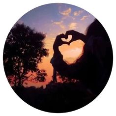 a person making a heart shape with their hands in front of the sun setting behind them