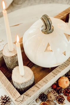 a white pumpkin sitting on top of a wooden tray filled with pine cones and candles