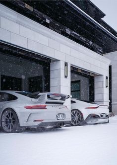 two white sports cars parked in front of a building on a snowy day with snow falling