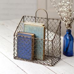 a blue vase with flowers and books in it next to a wire basket on a table