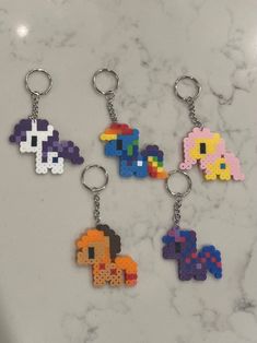 four pixel keychains are shown on a marble counter top, each with different colors and shapes