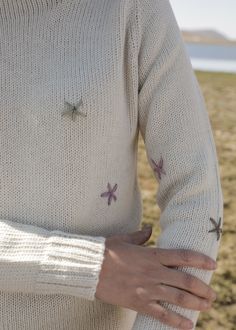 a woman with her hands on her hips wearing a sweater that has starfish embroidered on it