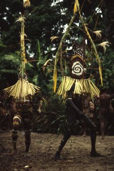 two people dressed in native garb and holding sticks