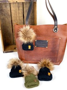 three knitted hats are sitting next to a brown bag and two other items in front of it