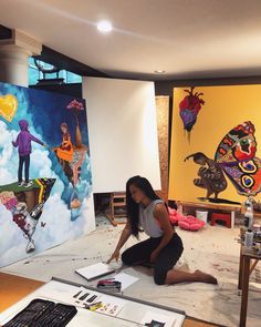 a woman sitting on the floor in front of two paintings and drawing with colored pencils