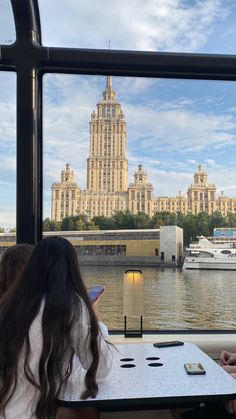 two people sitting at a table in front of a window looking out onto the water