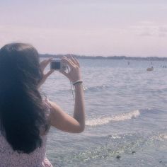 a woman taking a photo of the ocean with her cell phone