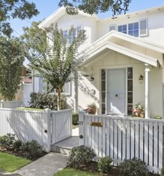 a white house with a picket fence and trees in the front yard on a sunny day