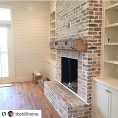 an empty living room with a brick fireplace and built - in shelving units on either side