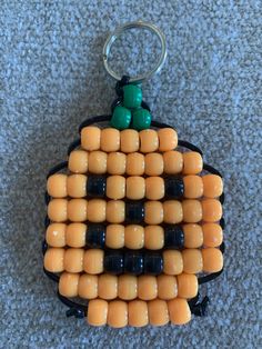 an orange and black corn cob keychain is on the floor with two green beads